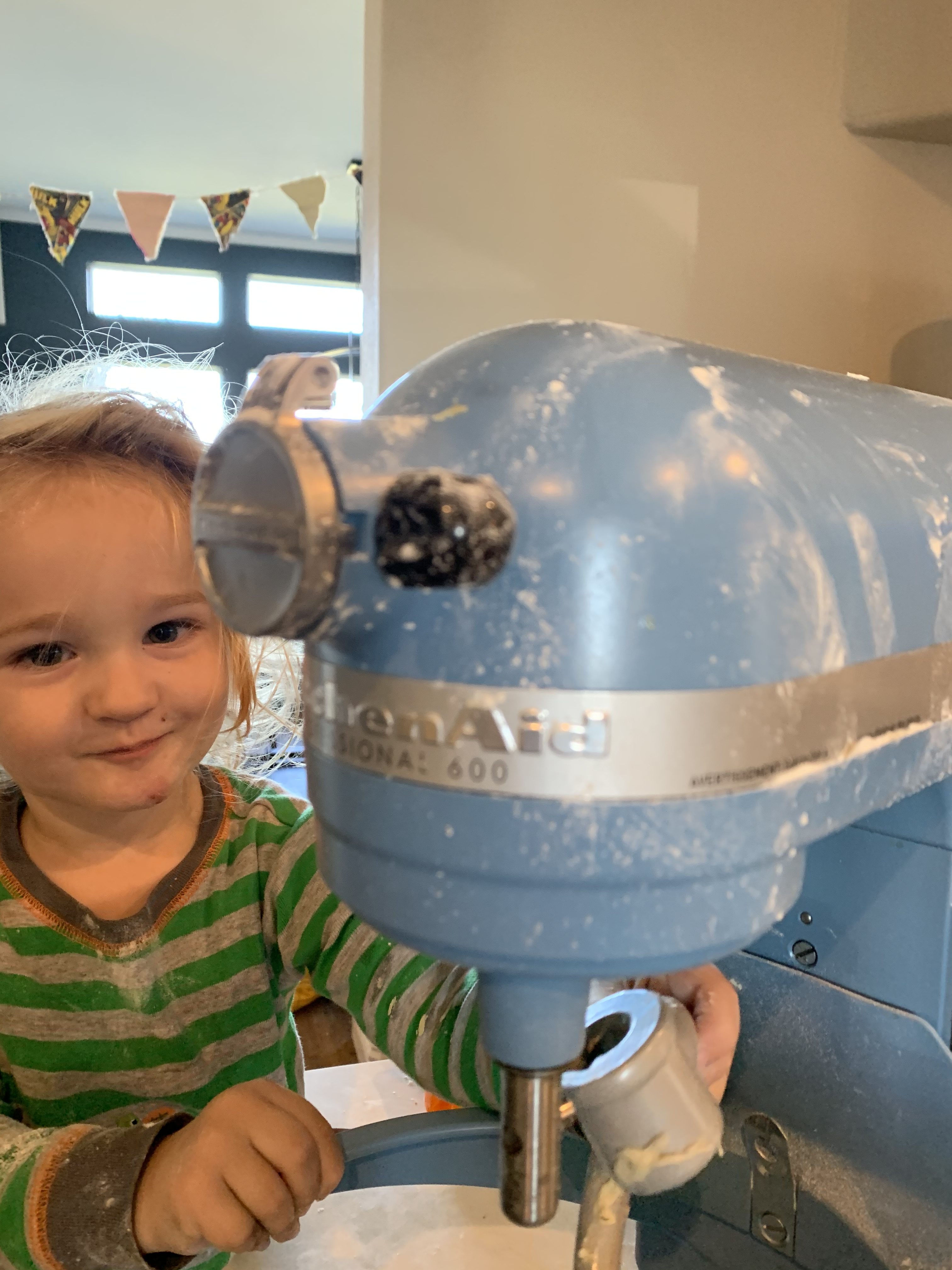 Smirking little boy trying to put attachment on the the baby blue kitchen aid mixer
